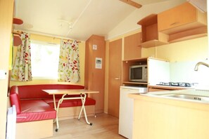A compact RV interior with a kitchenette, a dining area with a red bench, and a small table.