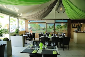 A restaurant with tables set for dining, a mural on the wall, and a view through the windows. - ZEcamping 4* piscine animations locatif TV BBQ clim 30m2 8 pers (Villeneuve-lès-Béziers)