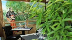 Un restaurante con un mural de un guitarrista, mesas con sillas y una planta en maceta al frente.