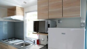 Cocina compacta con estufa a gas, microondas y refrigerador, que presenta gabinetes de madera y un ventanal.