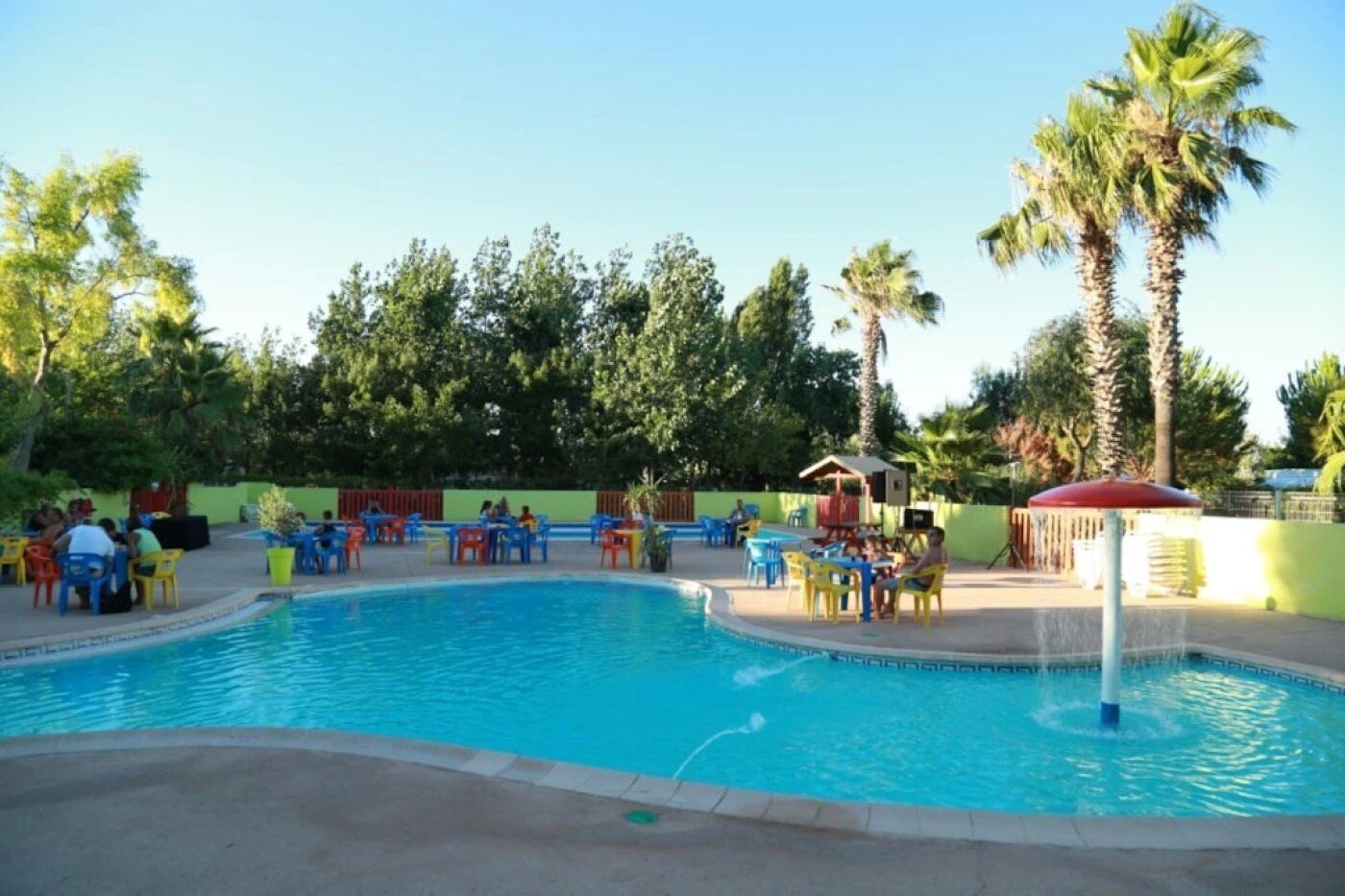 Ein Swimmingpool mit Liegestühlen und Tischen, umgeben von Palmen und Grünpflanzen.