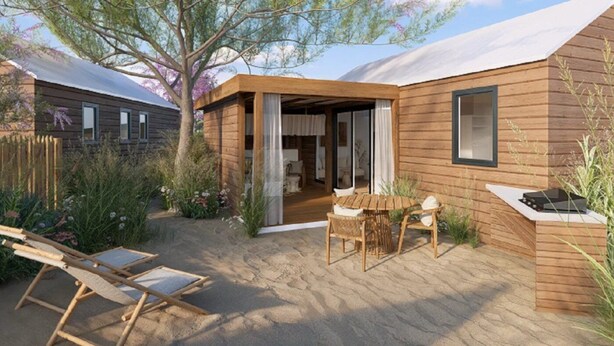 A wooden cabin with a covered patio, a dining area with a table and chairs, and a small garden with plants and flowers.