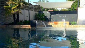 A pool area with a waterfall feature, surrounded by palm trees and a wall with the text "NATURE ZEN OCEAN".