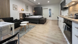 A modern, compact apartment with a kitchenette, a sofa bed, a dining area, and a small kitchen.