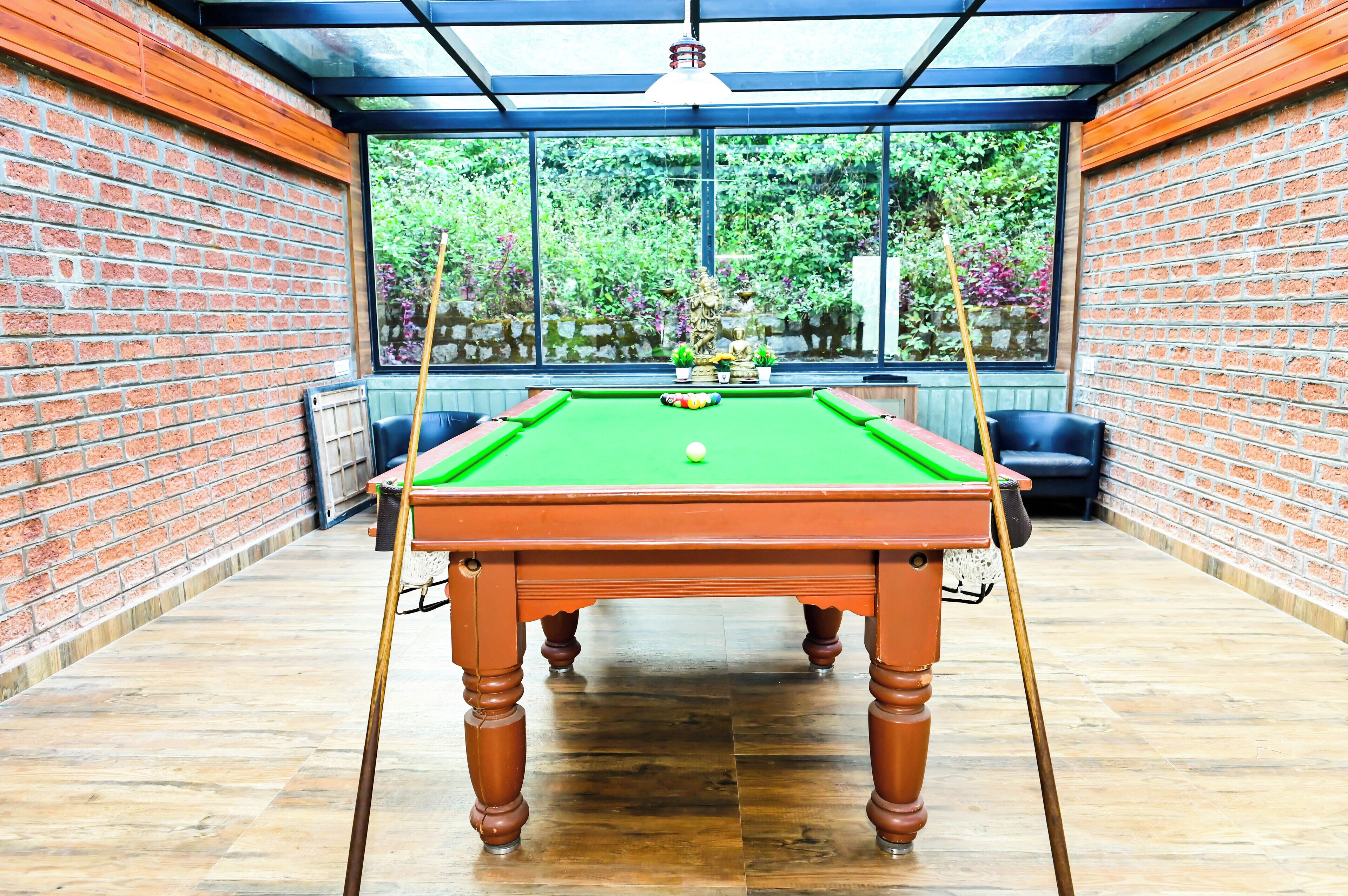 A pool table with a green felt surface, surrounded by brick walls and wooden flooring.