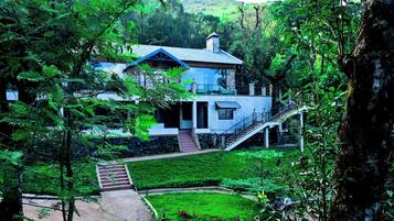 Una casa con una escalera que conduce a un balcón, rodeada de exuberante vegetación y un césped cuidado.