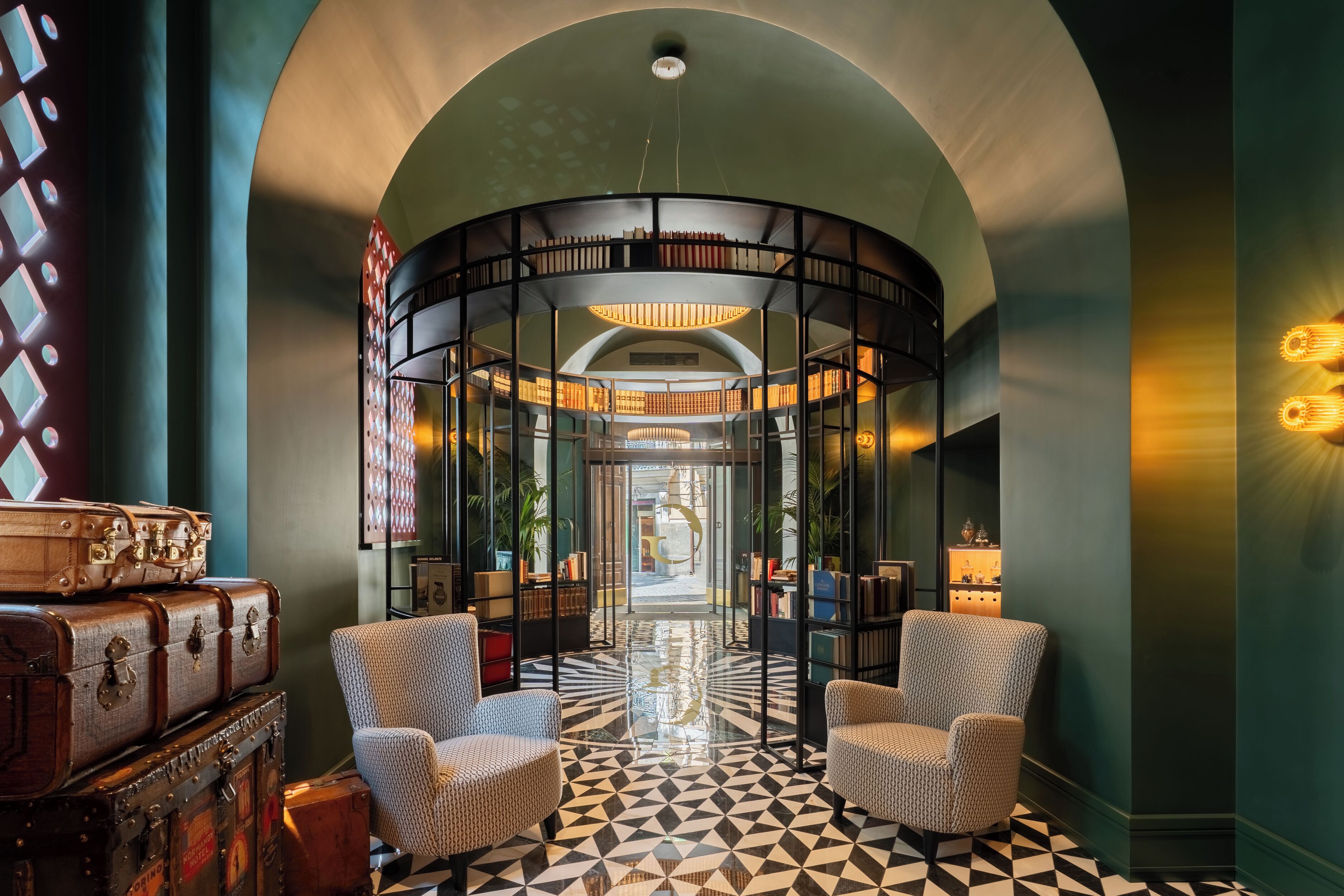 Un hall d’entrée doté d’un sol à motifs géométriques, d’une bibliothèque circulaire et de valises anciennes.