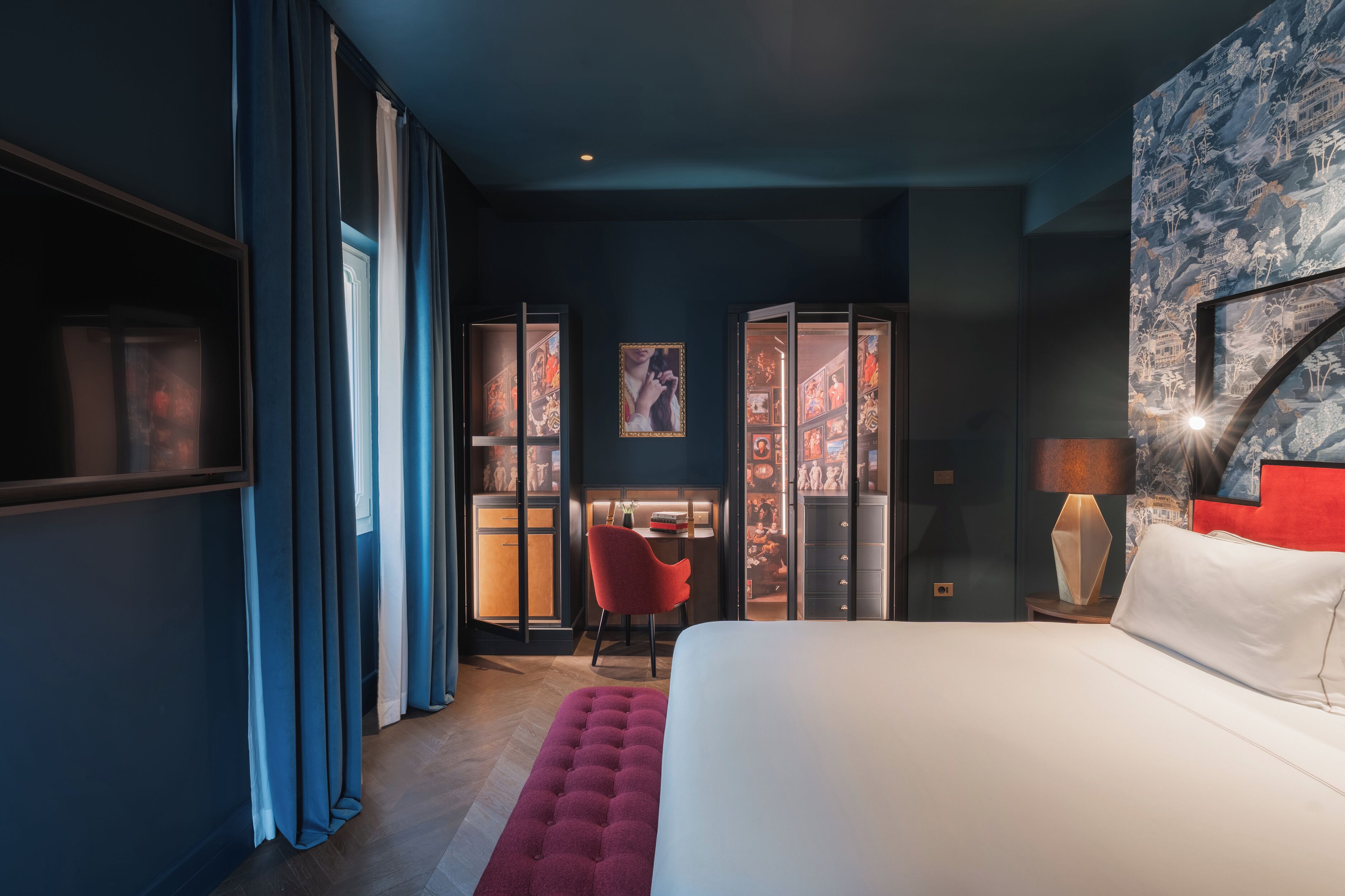 A modern hotel room with a large bed, a desk with a chair, and a wardrobe.