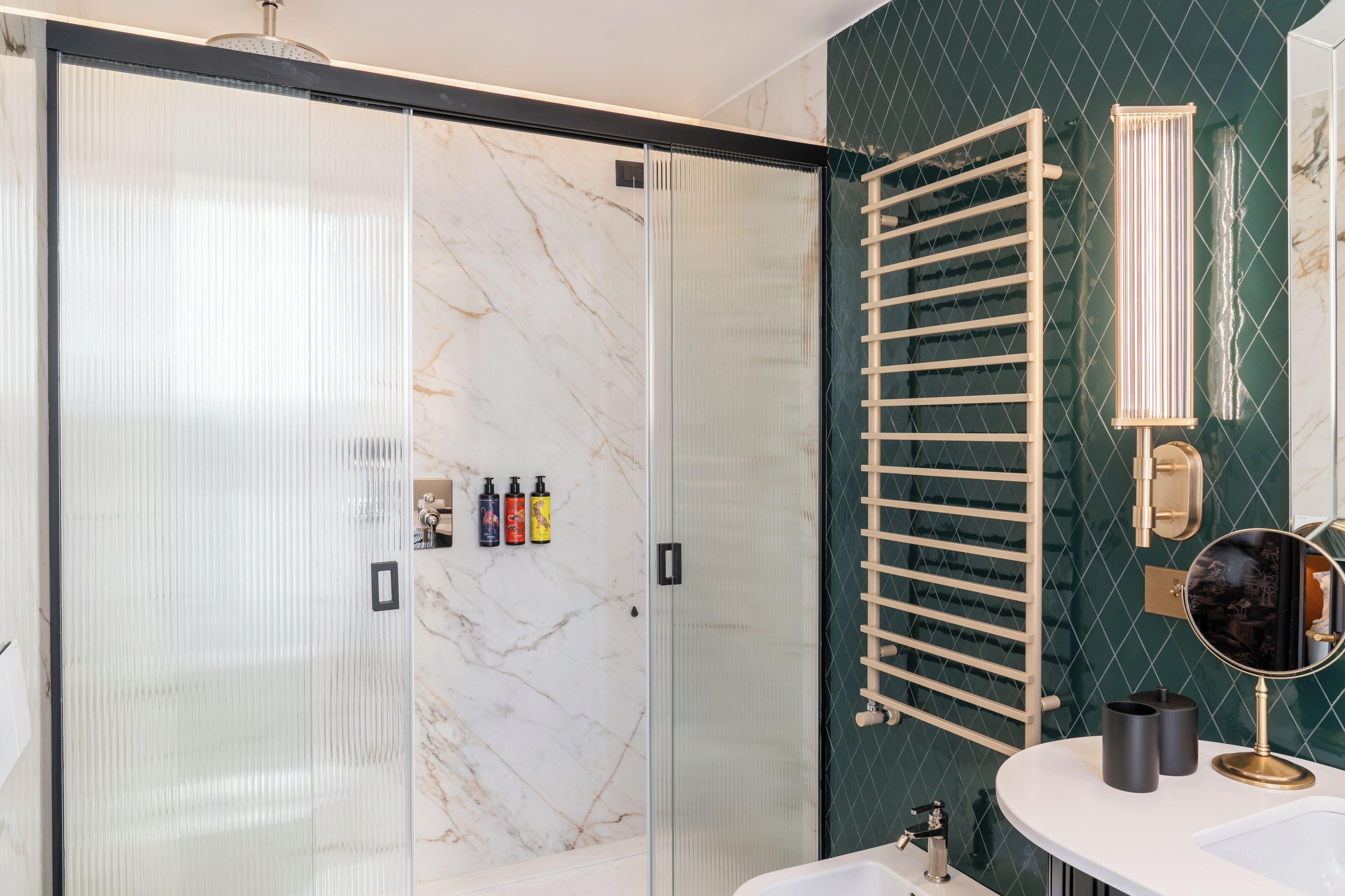 Un baño moderno con cabina de ducha de vidrio, un perchero de madera, un espejo redondo y un lavamanos blanco.