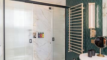Un baño moderno con cabina de ducha de vidrio, un perchero de madera, un espejo redondo y un lavamanos blanco.