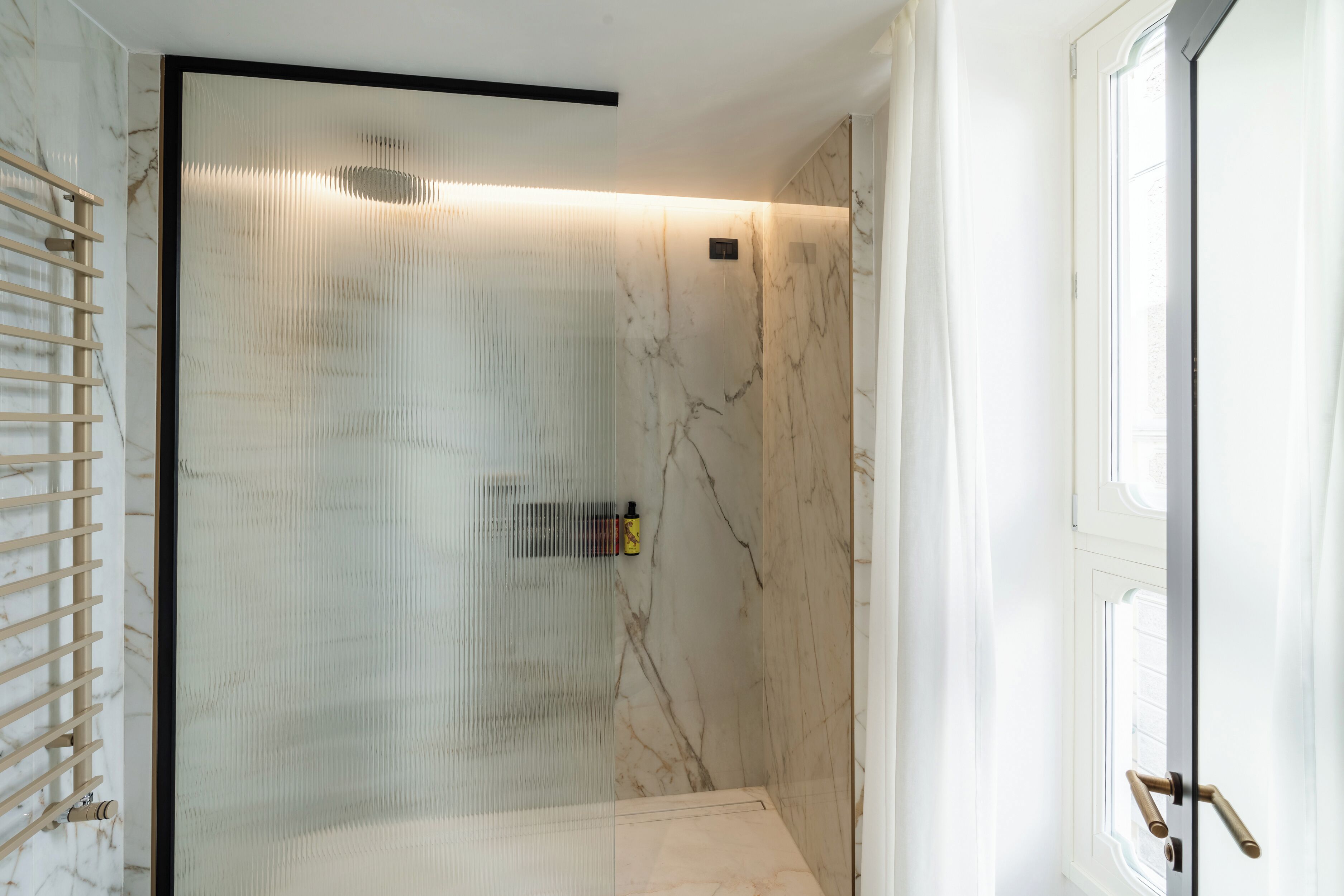Un baño con cabina de ducha de vidrio, un perchero y una ventana.
