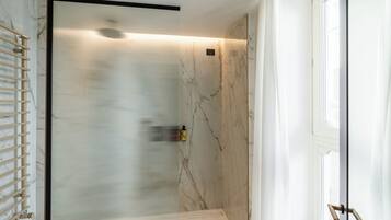 Un baño con cabina de ducha de vidrio, un perchero y una ventana.