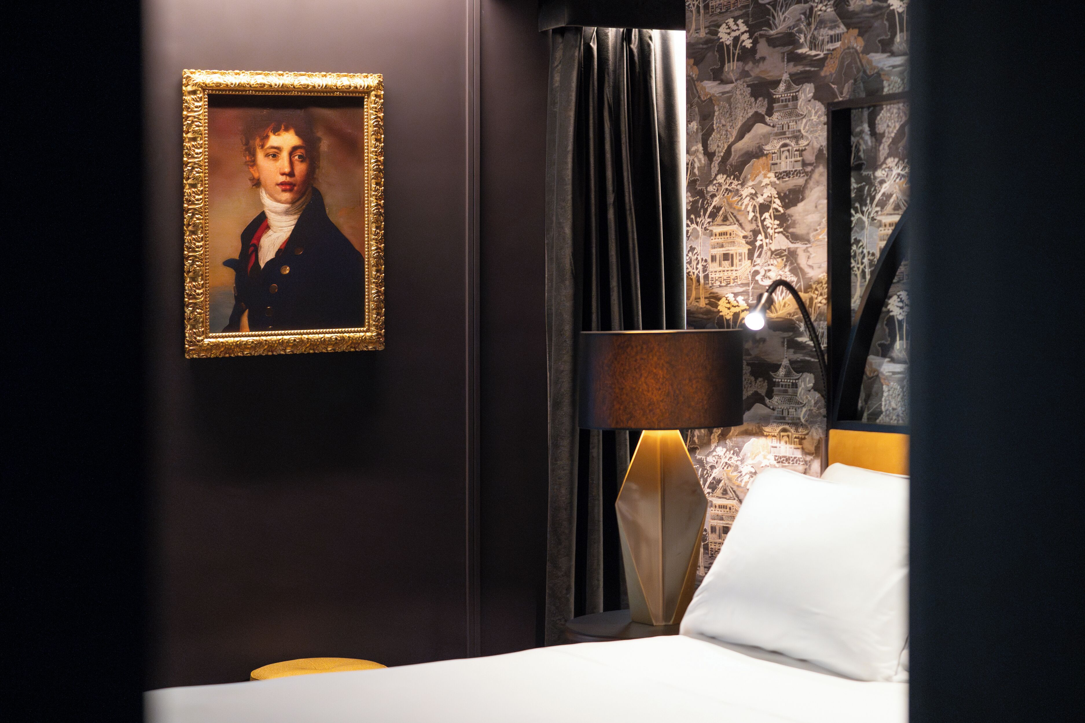 A hotel room with a framed portrait on the wall, a lamp, and a bed with white bedding.