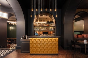 A bar area with a geometric patterned counter, hanging lights, and shelves of bottles.