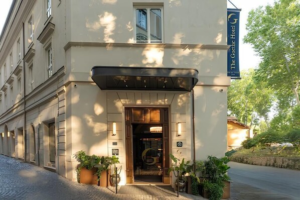 A hotel entrance with a wooden door, potted plants, and a sign indicating 'The Goth Hotel.'