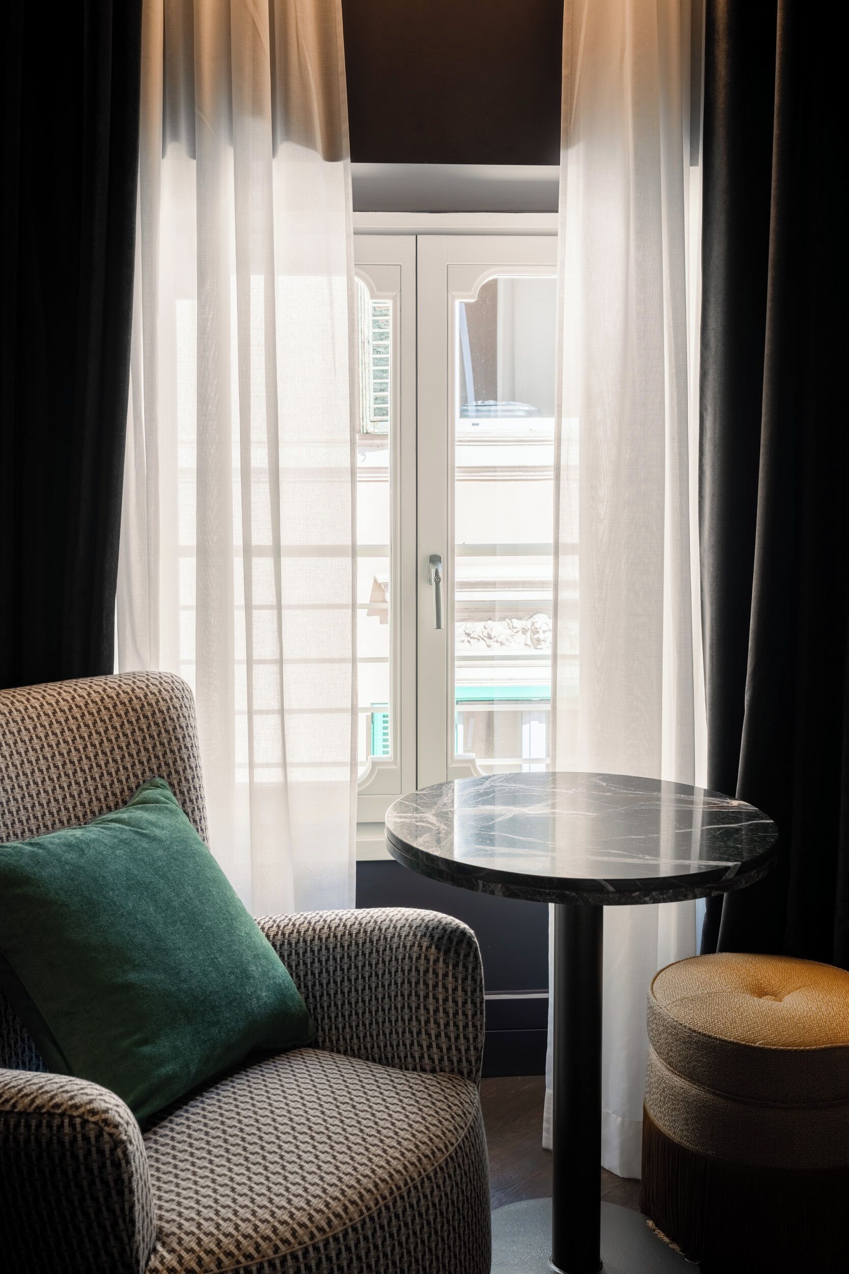 A room with a patterned sofa, a round table, and sheer curtains.