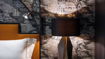 Habitación de hotel con cama, mesita de noche con lámpara y pared con un mural detallado.