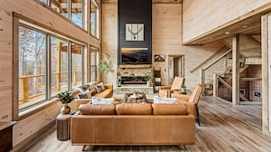A spacious living room with a large sofa, a fireplace, and a view of the outdoors through large windows. - Top 1%, Pickleball, Sauna, Hot Tub, Near Dollywood (Sevierville)