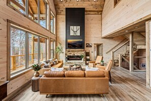 Un salon spacieux, doté d’un grand canapé, d’une cheminée et offrant une vue sur l’extérieur grâce à de grandes fenêtres.