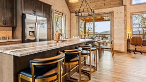 A kitchen with dark cabinets, a stainless steel refrigerator, a marble countertop, and a bar area with stools. - Top 1%, Pickleball, Sauna, Hot Tub, Near Dollywood (Sevierville)