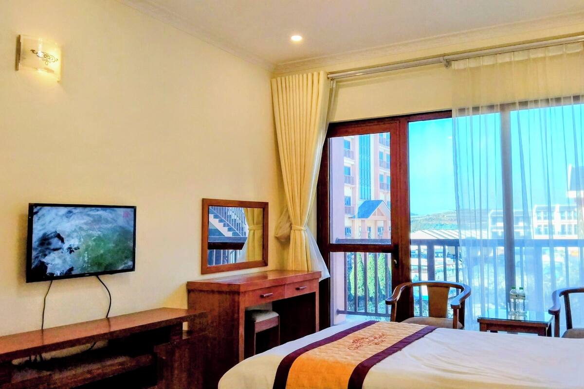 Une chambre d’hôtel avec un lit, un bureau, une chaise, une télévision et une fenêtre avec des rideaux.