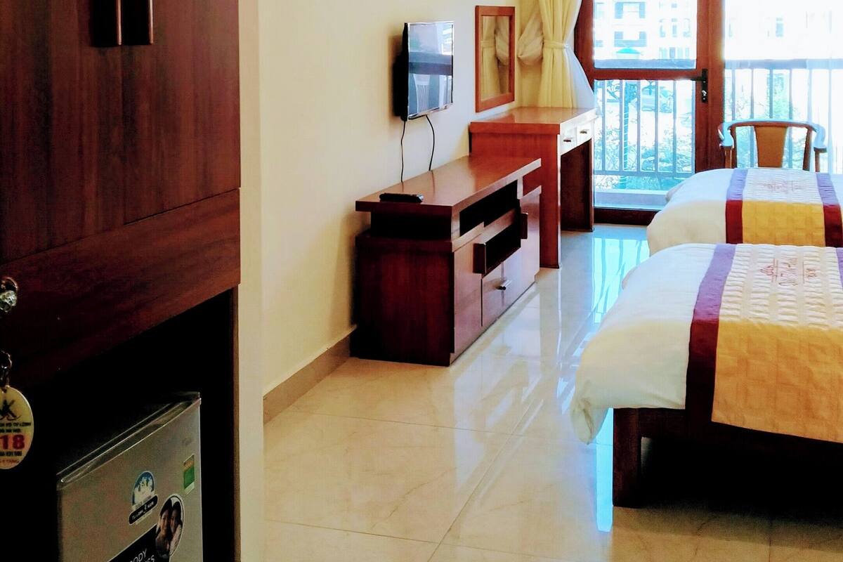 Une chambre d’hôtel avec une armoire en bois, un bureau avec une télévision, un lit avec une couette et un balcon avec vue.