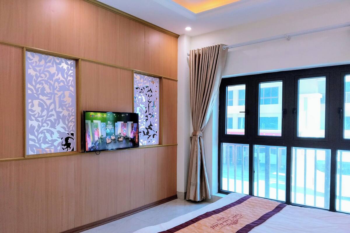 Une chambre d’hôtel avec un grand lit, un téléviseur fixé au mur et une fenêtre avec des rideaux.