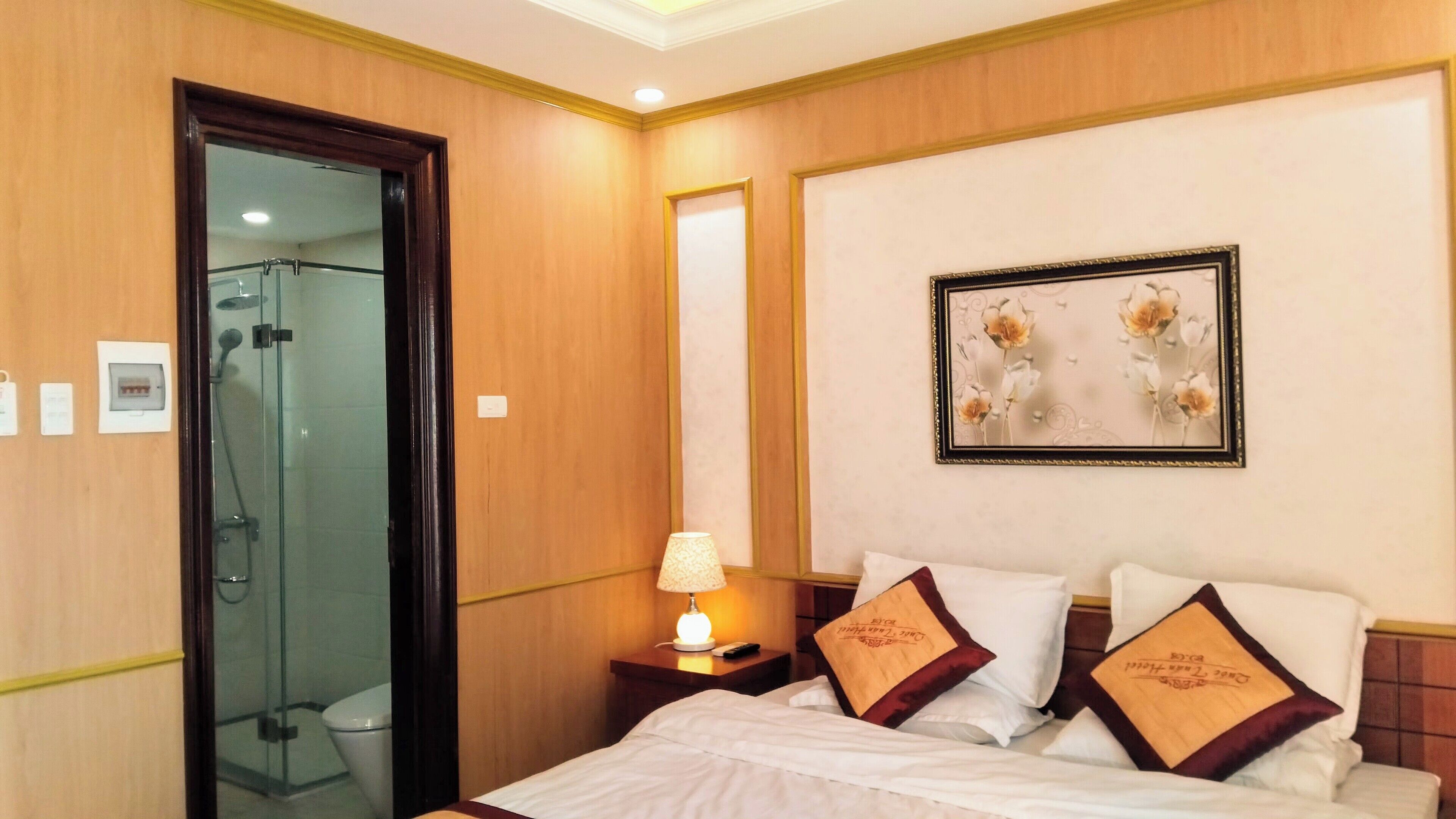 A hotel room with a bed, a nightstand, a lamp, a framed picture on the wall, and a shower area.