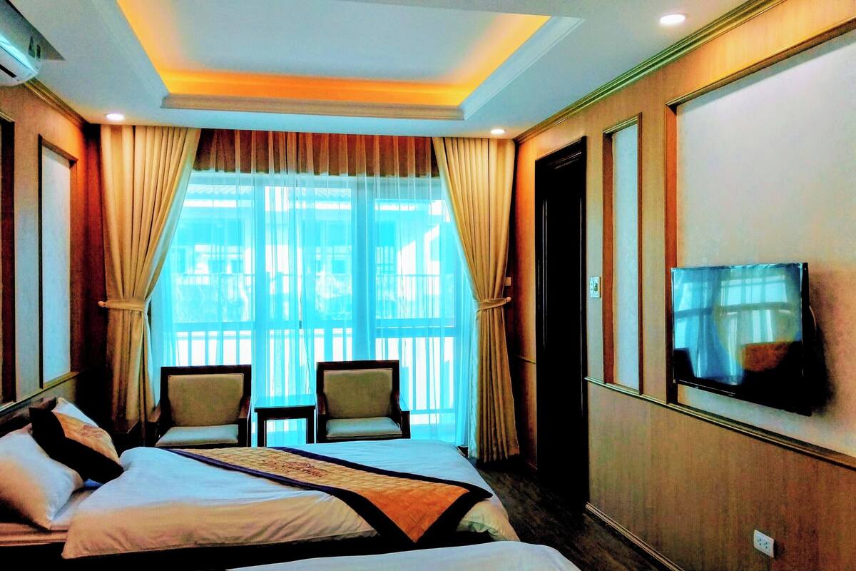 Une chambre d’hôtel avec un lit, deux chaises, un téléviseur et une grande fenêtre avec des rideaux.