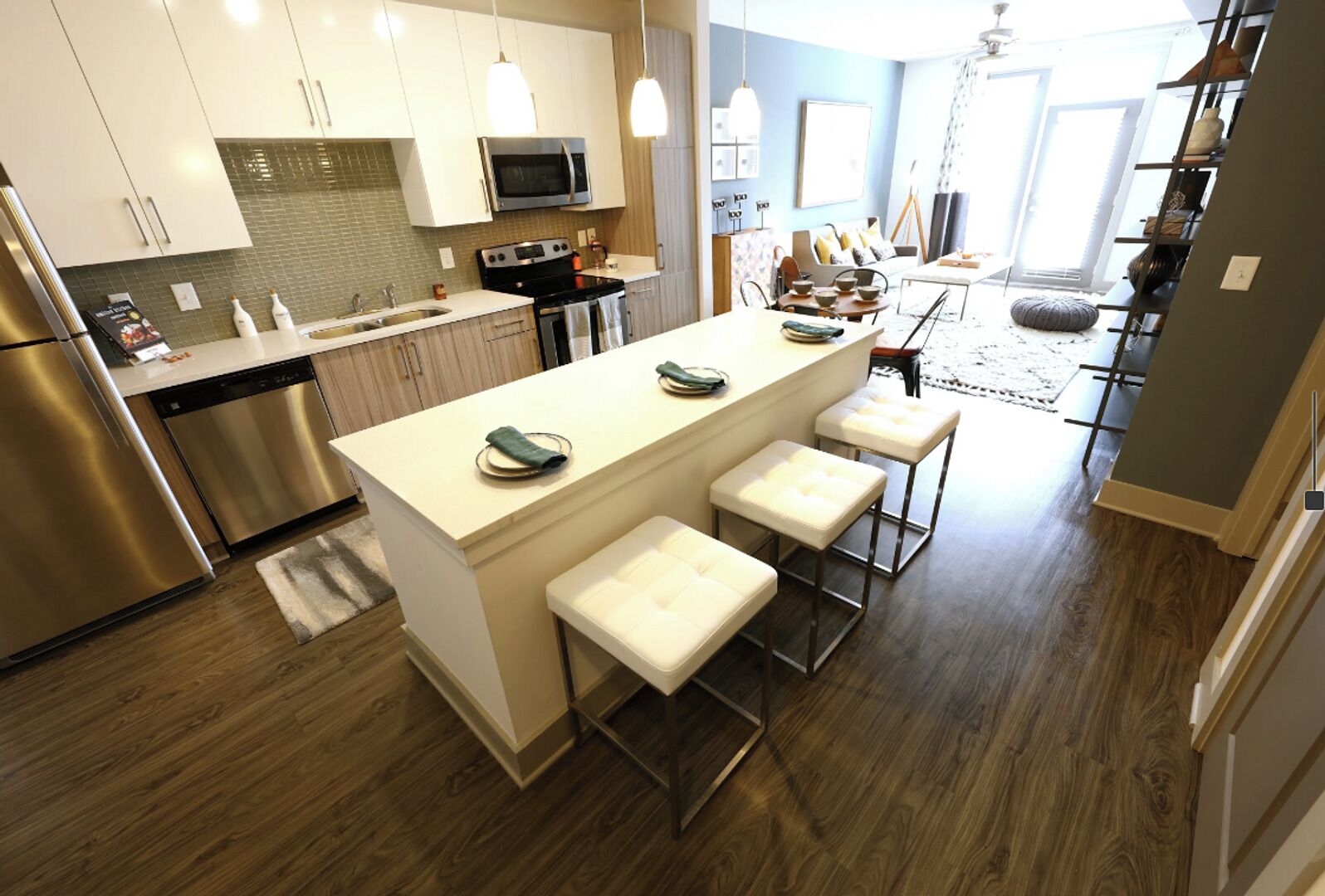 A modern kitchen with stainless steel appliances, a central island with bar stools, and a dining area with a view.