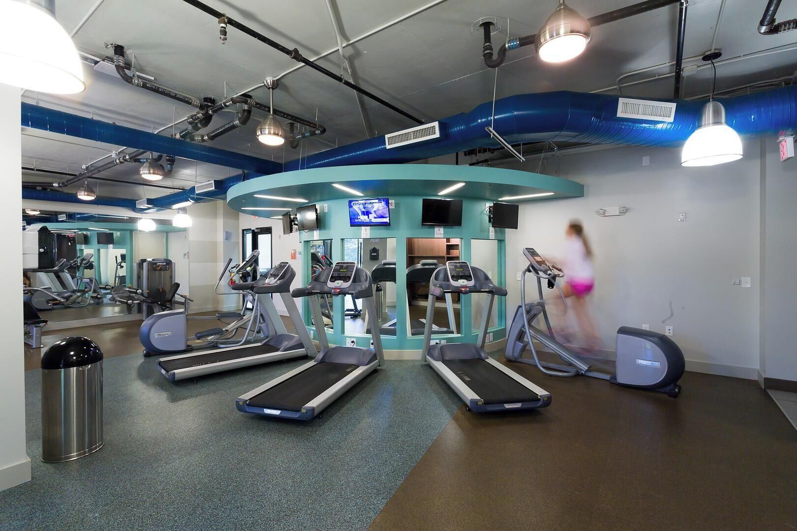 Een sportschool met loopbanden, elliptische trainers en een spiegelwand.
