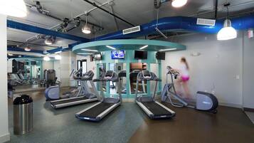 Een sportschool met loopbanden, elliptische trainers en een spiegelwand.