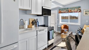 A modern kitchen with white cabinetry, a stove, and a window with a view of a lake. - Cozy Waterfront Cottage (Noank)