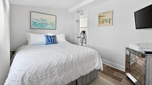 A bedroom with a bed, a TV, a dresser, and two paintings on the wall. - Cozy Waterfront Cottage (Noank)