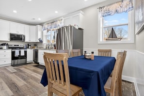 A modern kitchen with white cabinets, stainless steel appliances, and a dining area with a blue tablecloth and wooden chairs. - 11 Bedroom Tranquil Waterfront Getaway (Noank)
