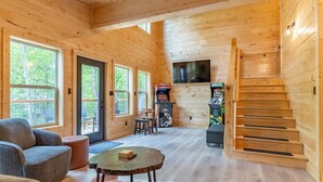 L'intérieur d'un chalet en bois, avec un canapé, une table ronde, un escalier et un téléviseur fixé au mur.