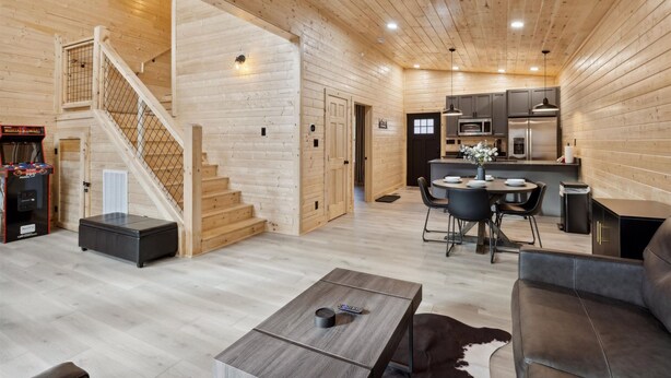 Un vaste espace de vie comprenant un escalier en bois, une table à manger avec des chaises, un canapé et un coin cuisine équipé d’appareils électroménagers modernes.