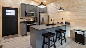 Une cuisine moderne avec des meubles gris, des appareils en acier inoxydable, un îlot central doté de tabourets de bar et des murs en bois.
