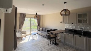 A spacious kitchen with a dining area, a sofa, and a large window with curtains.