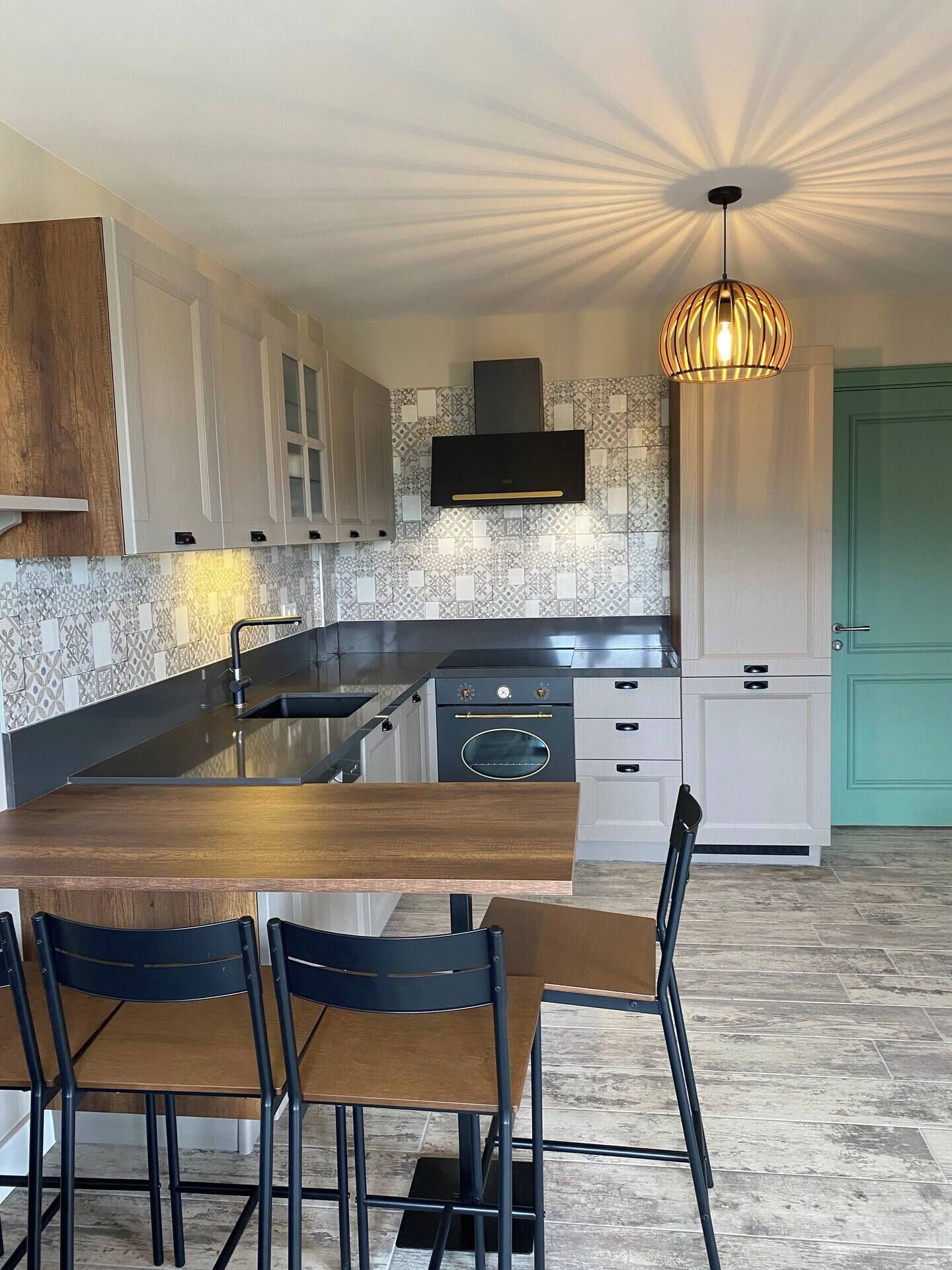 A modern kitchen with a central island, white cabinets, a built-in oven, and a hanging light fixture.