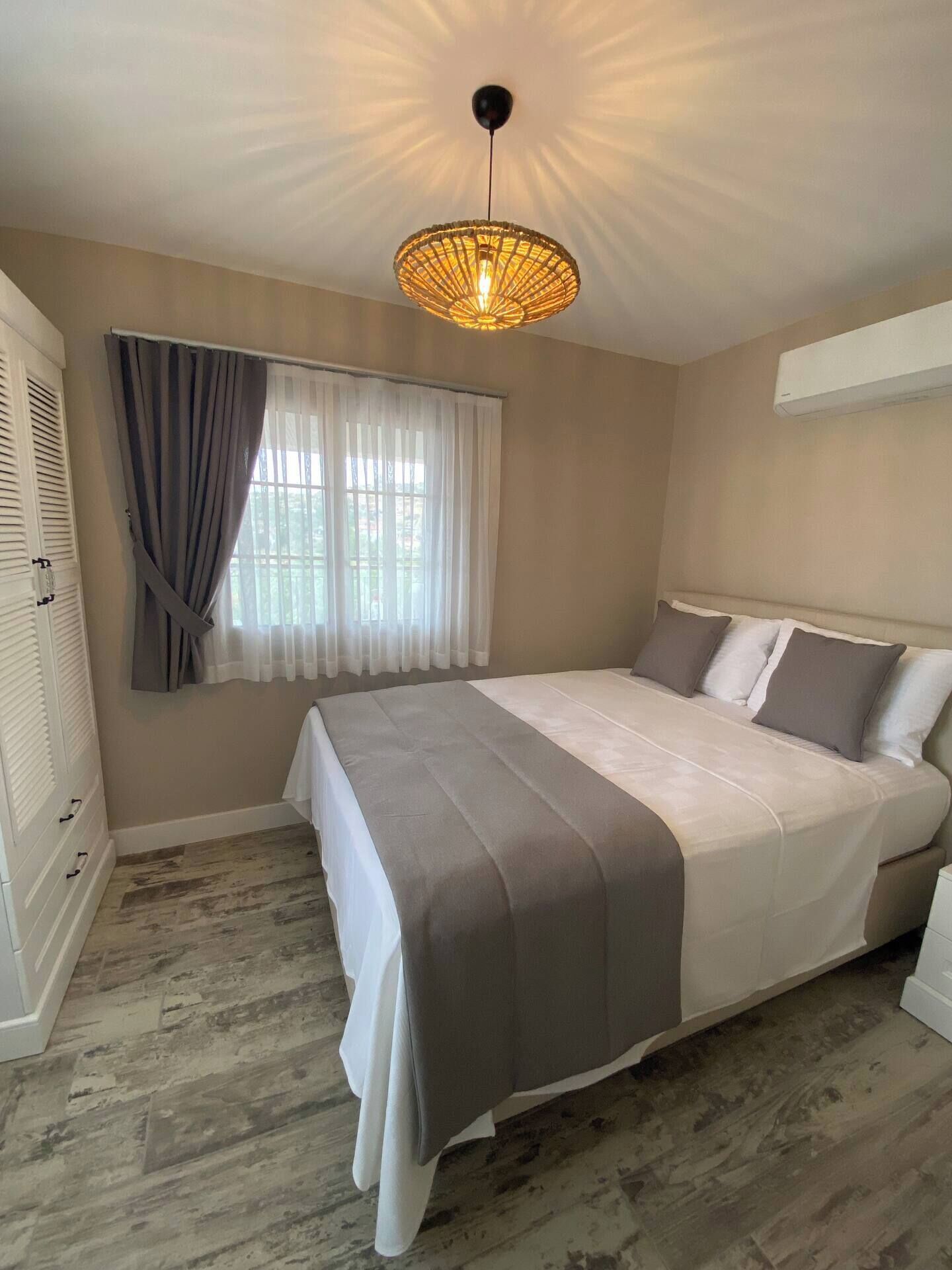 A bedroom with a bed, a window with curtains, a ceiling light fixture, and an air conditioning unit.