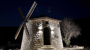 A stone windmill with a wooden structure at night, illuminated by lights.