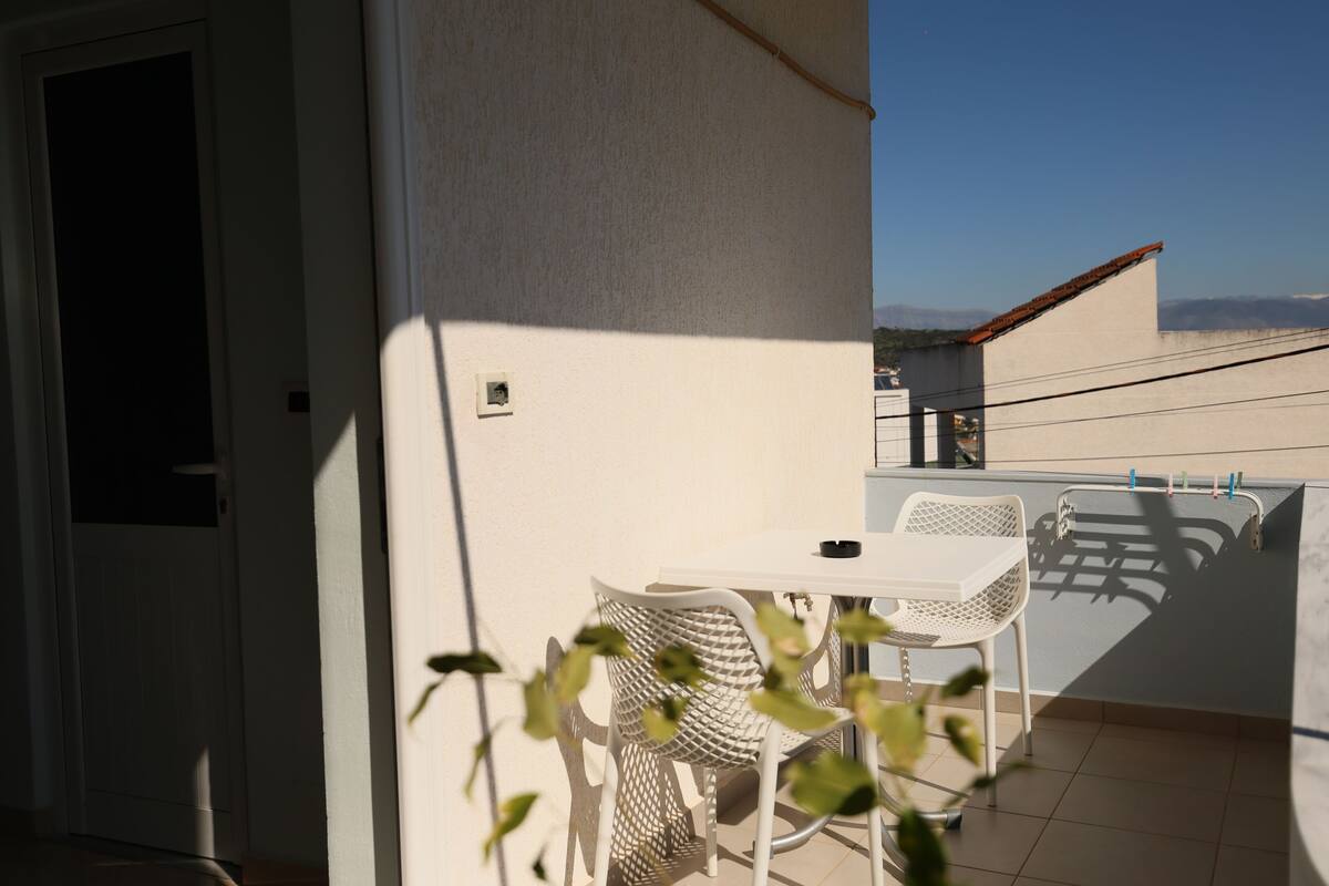 A balcony with a white table and chairs, a door, and a view of the cityscape.