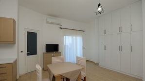 A room with a dining table, chairs, a television, cabinets, and a window with curtains. - Michelle Apartments (Ksamil)
