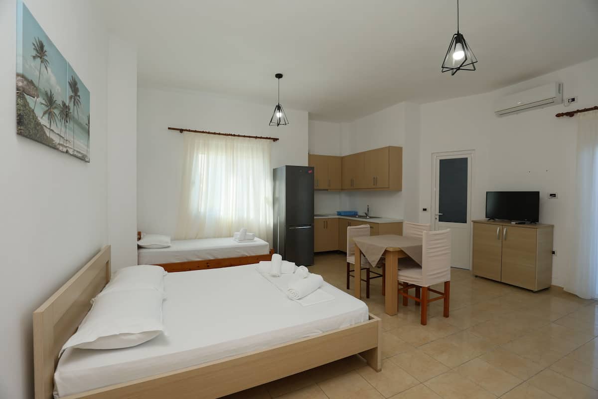 A hotel room with a bed, a desk, a chair, a television, a refrigerator, and a kitchen area.