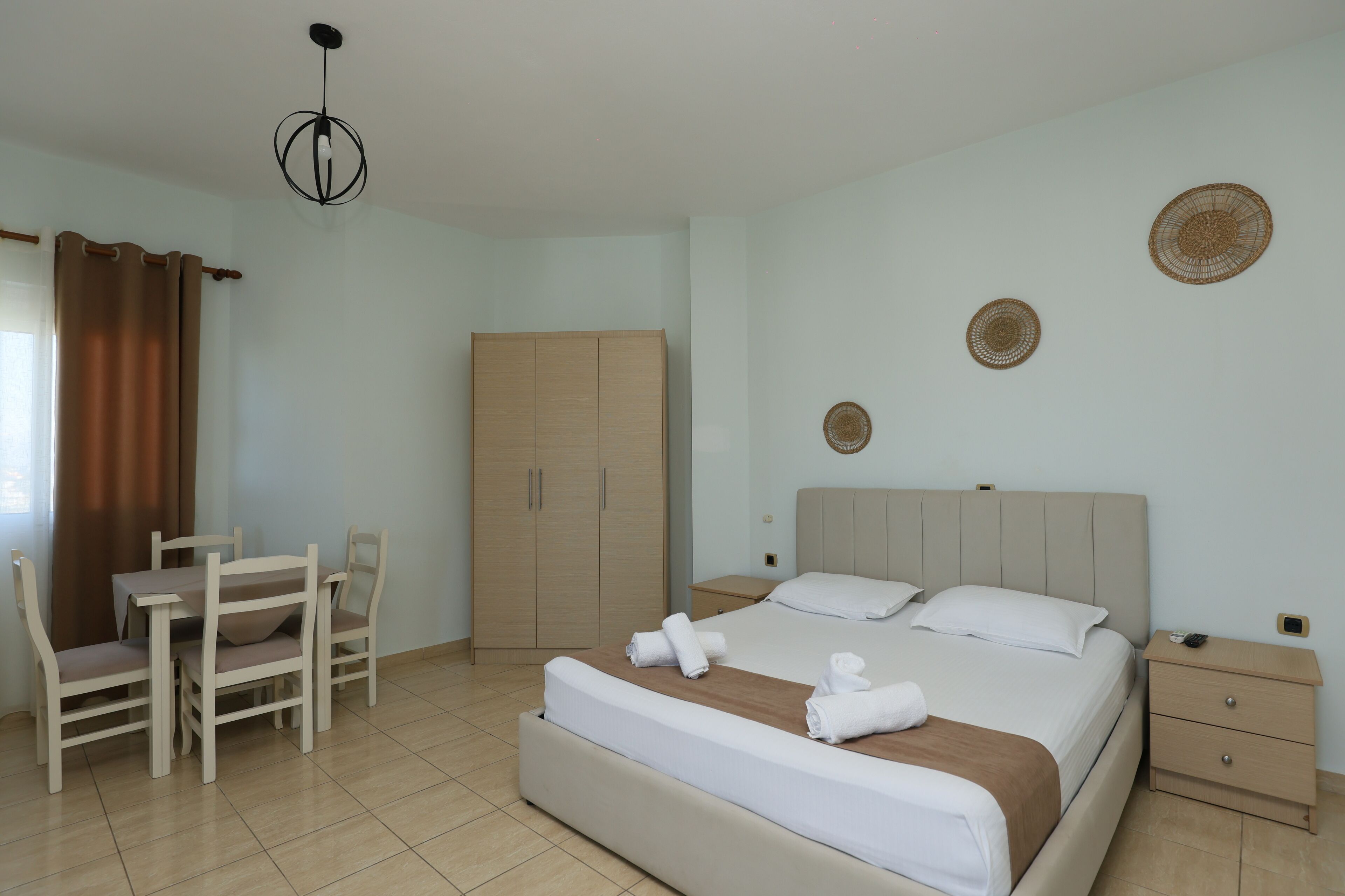 A bedroom with a bed, bedside tables, a wardrobe, a desk with chairs, and a hanging light fixture.