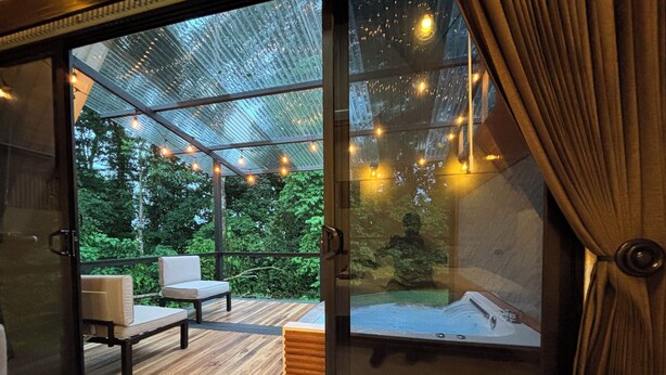 Una terraza moderna al aire libre con piso de madera, un área de estar con sofá y sillones, y un jacuzzi.
