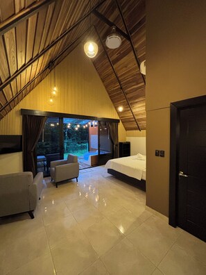 A spacious bedroom with a large bed, a seating area with a sofa and chairs, and a view of the outdoors through large windows. - River Paradise Cabin with Private Jacuzzi (Provincia de Alajuela)