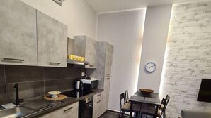 A modern kitchen with grey cabinets, a built-in oven, and a dining area with a table and chairs. - Be Magenta Art Home - Yellow style (Magenta)