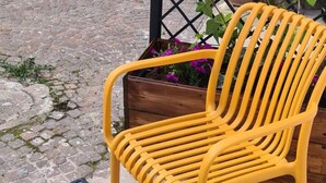 A yellow chair and a small table with a bowl on it, placed on a cobblestone surface. - Be Magenta Art Home - Yellow style (Magenta)